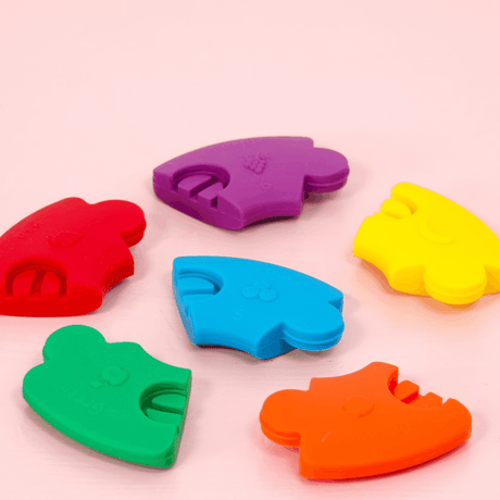 Kolorowe gryzaki silikonowe Jellystone Designs w kształcie owoców dla niemowlaka, łączące zabawę z ulgą i edukacją.